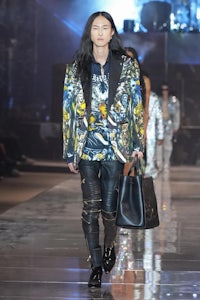 a man with long hair walks down the runway