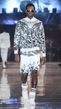 a man walking down the runway in a black and white sweater and shorts