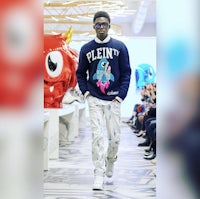 a man walking down a runway wearing a sweater with a cartoon character on it