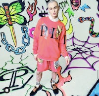 a man in an orange sweatshirt standing in front of a graffiti wall