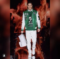 a man on a runway wearing a green jacket and white pants