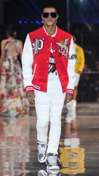 a model wearing a red jacket and white pants on the runway