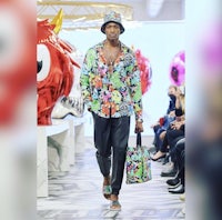 a man in a colorful shirt walks down the runway