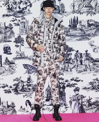 a man standing in front of a wallpapered wall